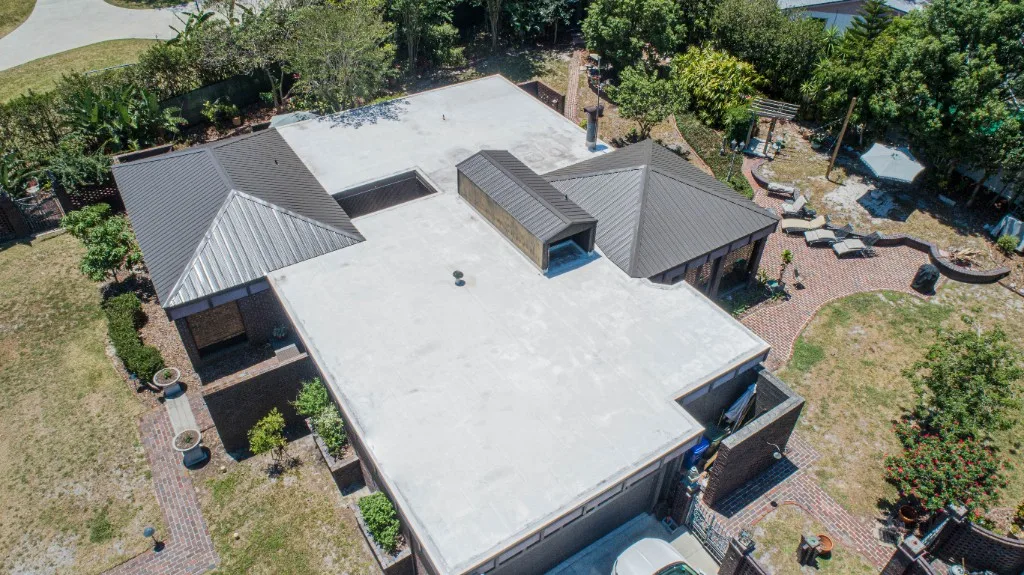 Aerial view of a completed Stronghold Roofing white TPO flat roof with dark bronze standing-seam metal accent sections on a Florida mid-century modern home