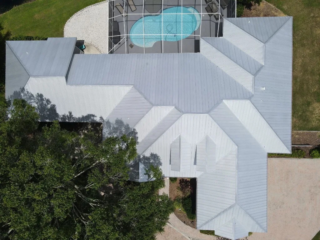 Top-down aerial view of a completed Stronghold Roofing white standing-seam metal roof over a Florida home with a screened pool cage in the backyard